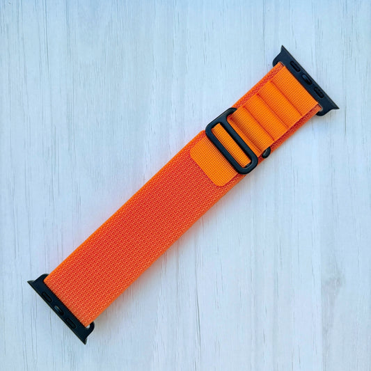 Orange Apple watch strap with black buckle and black connectors on a white wooden background.