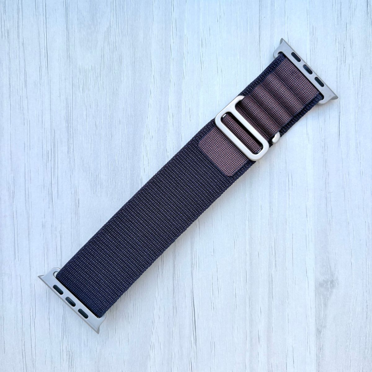 Indigo Alpine Loop Apple watch band with silver buckle on white wooden background.