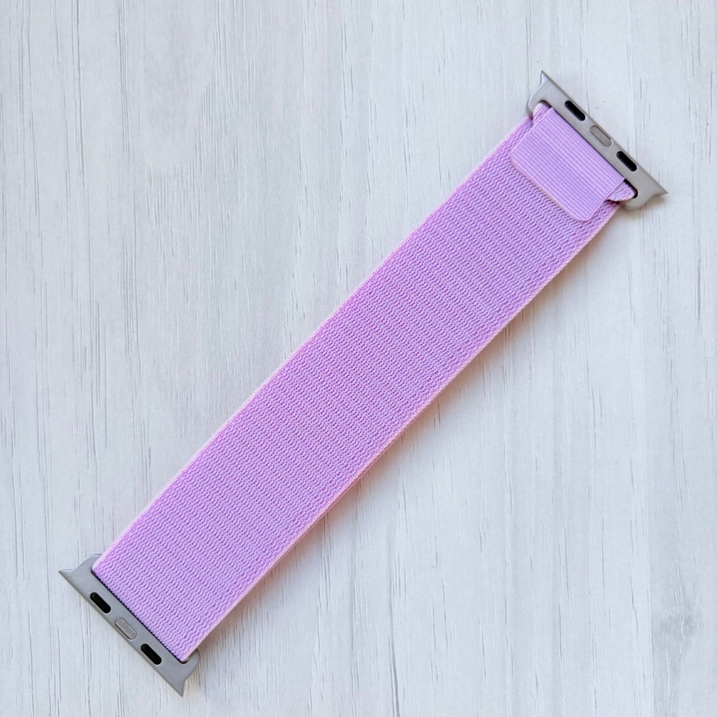Lavender Alpine Loop woven Apple watch strap on a light wooden surface
