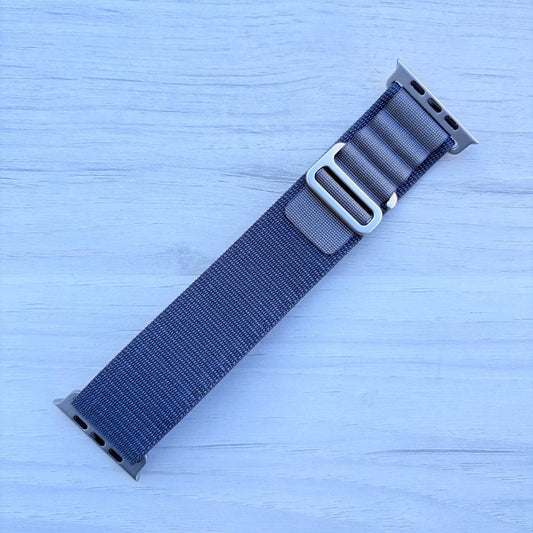 Blue Alpine Loop Apple Watch Strap with silver buckle on a light blue wooden surface