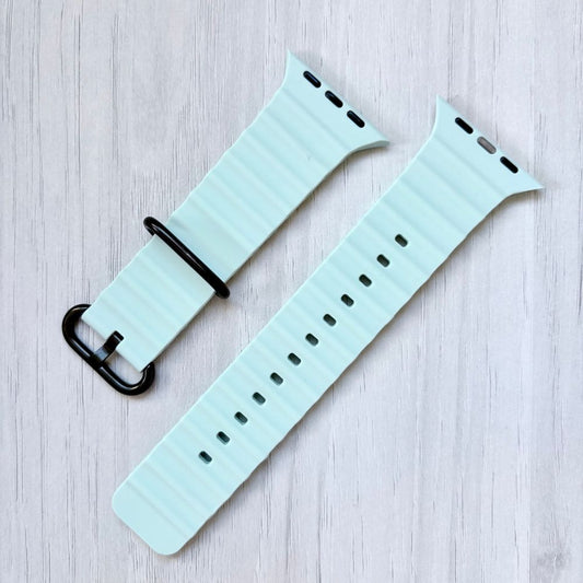 Ice blue Ocean band Apple watch strap with black buckle on a light wooden surface