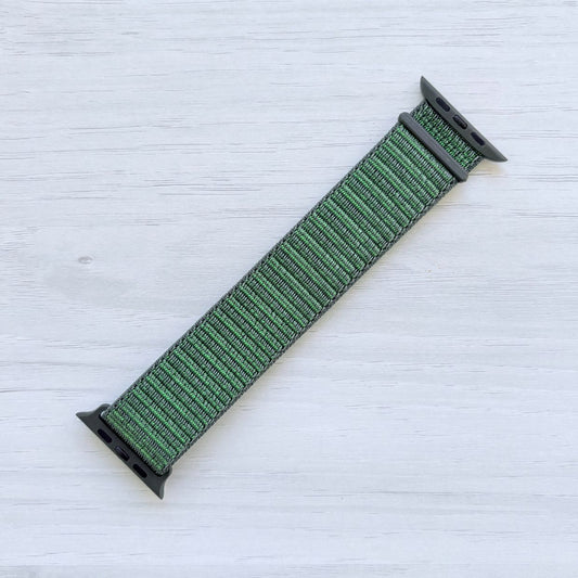 Green apple watch strap with green hardware on a light wooden surface