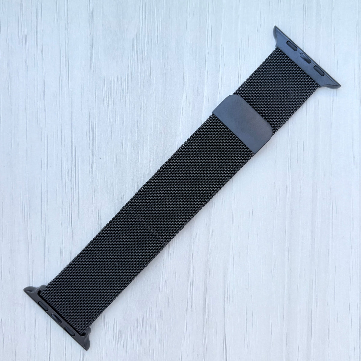 Black Milanese loop for Apple Watch strap on a light blue textured background