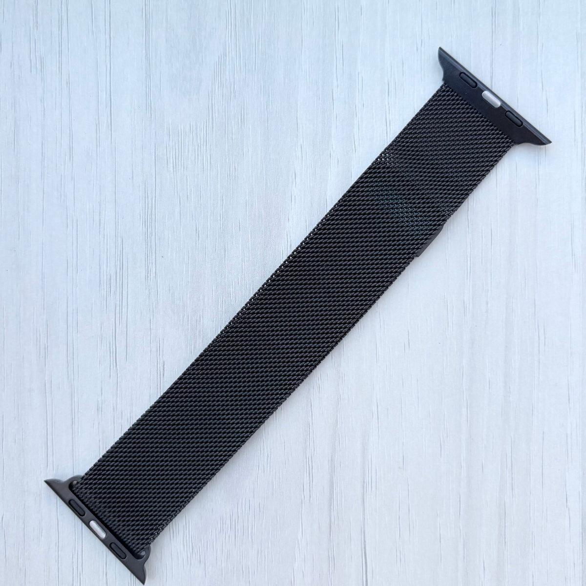 Black mesh watch strap on a light blue wooden surface