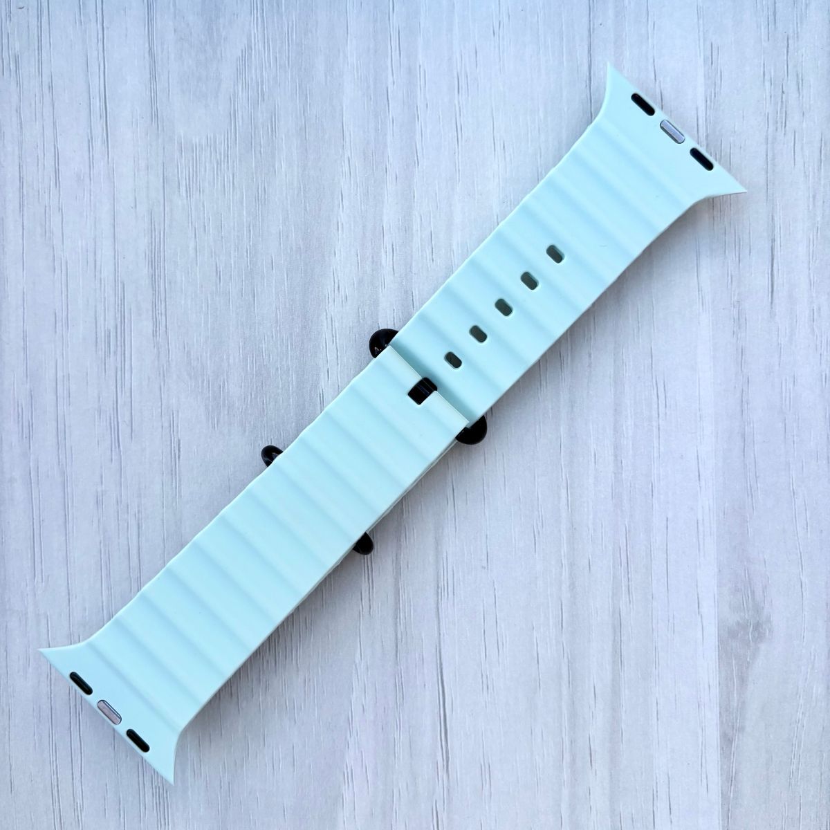 Apple watch Ocean Band in Ice Blue with black buckle on a White wooden background
