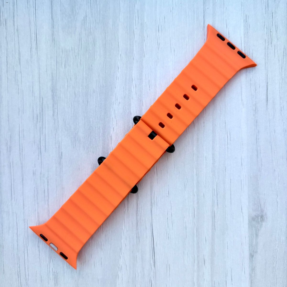 Apple watch Ocean Band in Orange with black buckle on a White wooden background