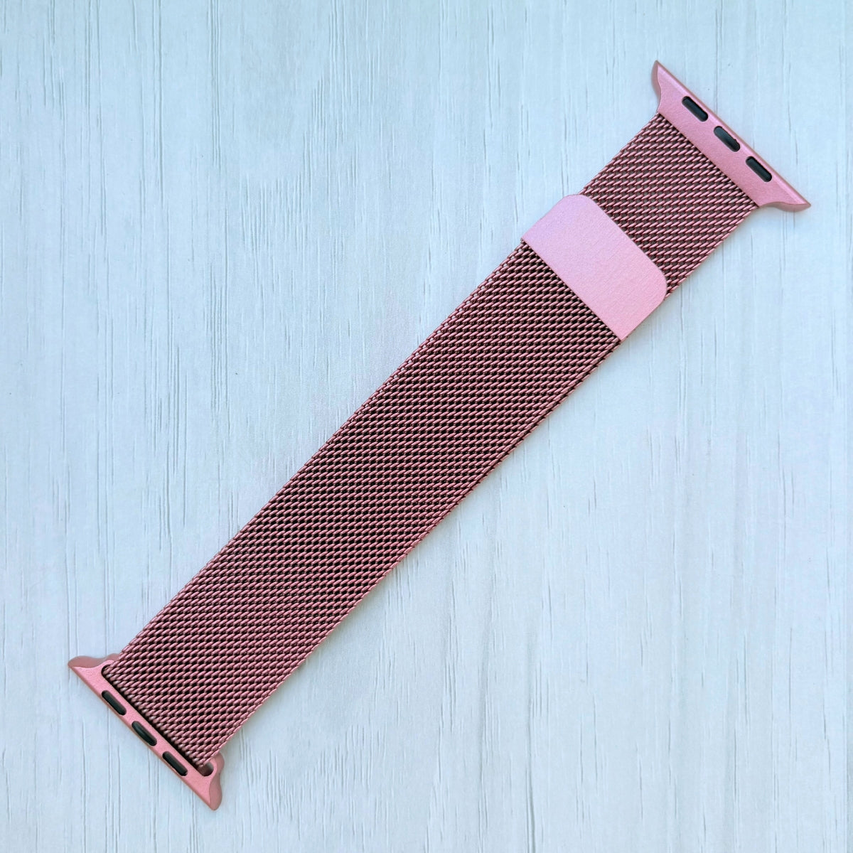 Pink Milanese Apple watch strap on a White wooden surface