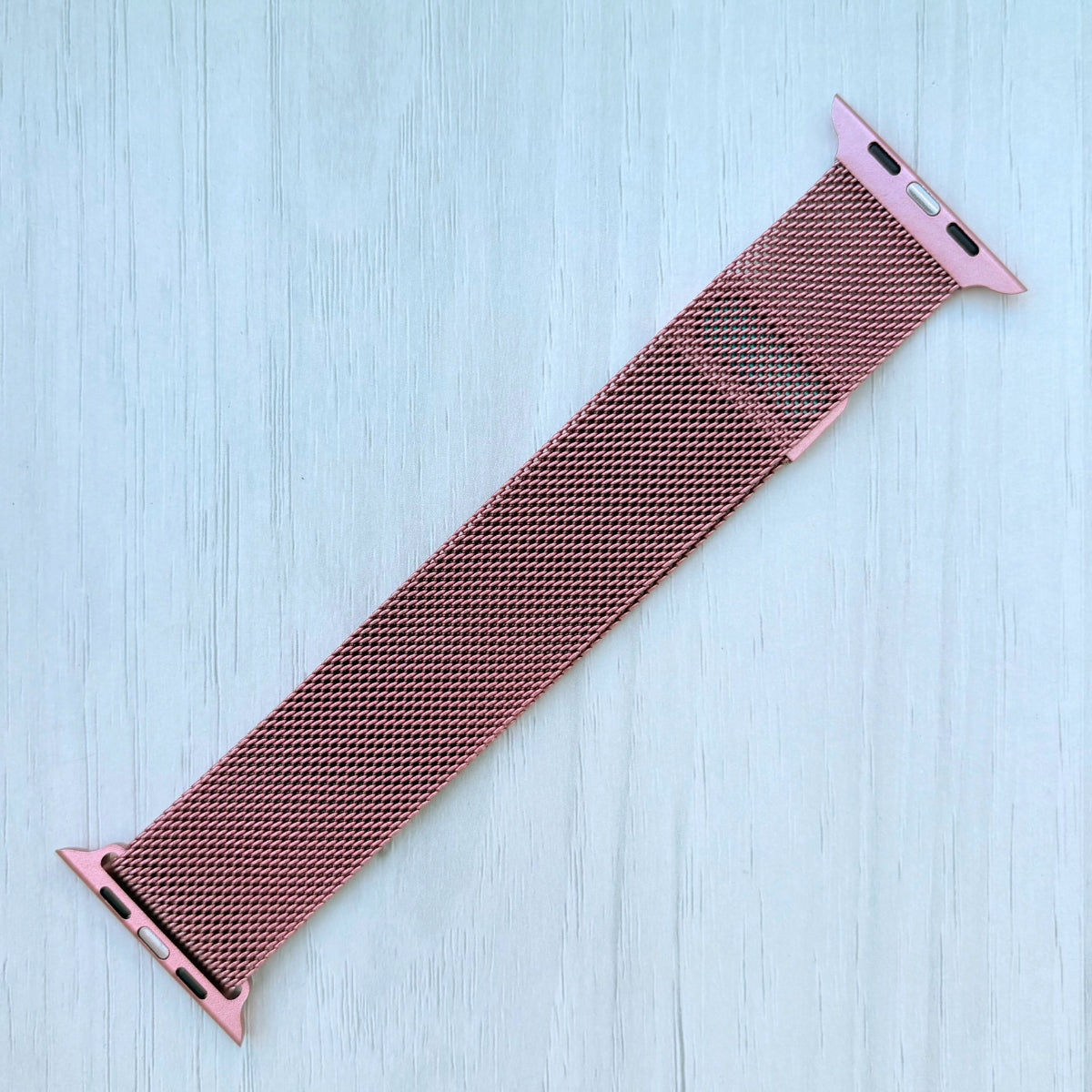 Pink Milanese Apple watch strap on a White wooden surface