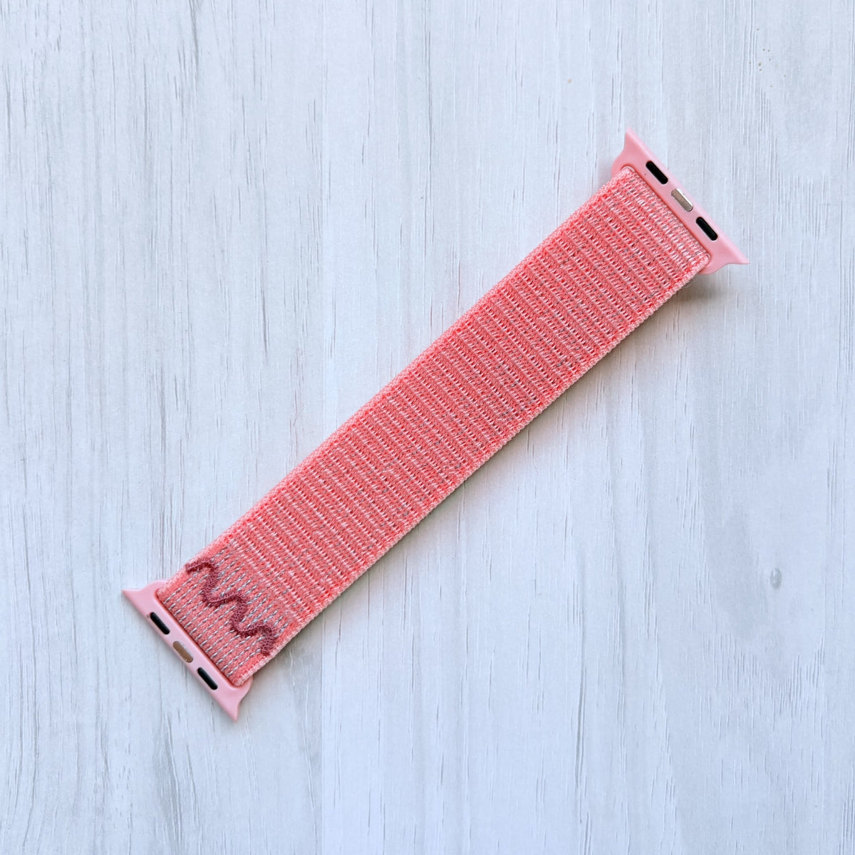 Alpenglow Pink Apple watch nylon band on a light wooden surface, back side.
