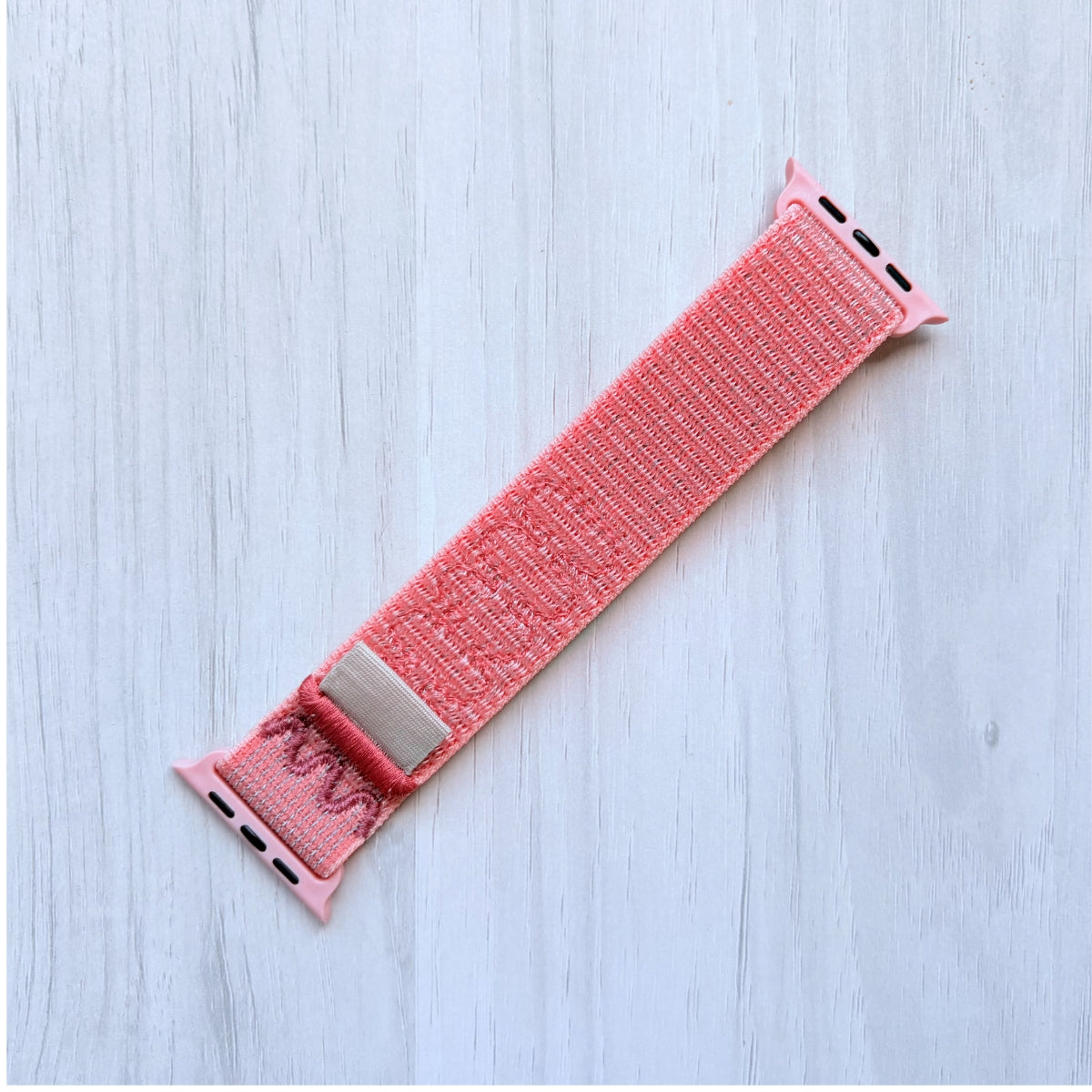 Alpenglow Pink Apple watch nylon band on a light wooden surface, front side.