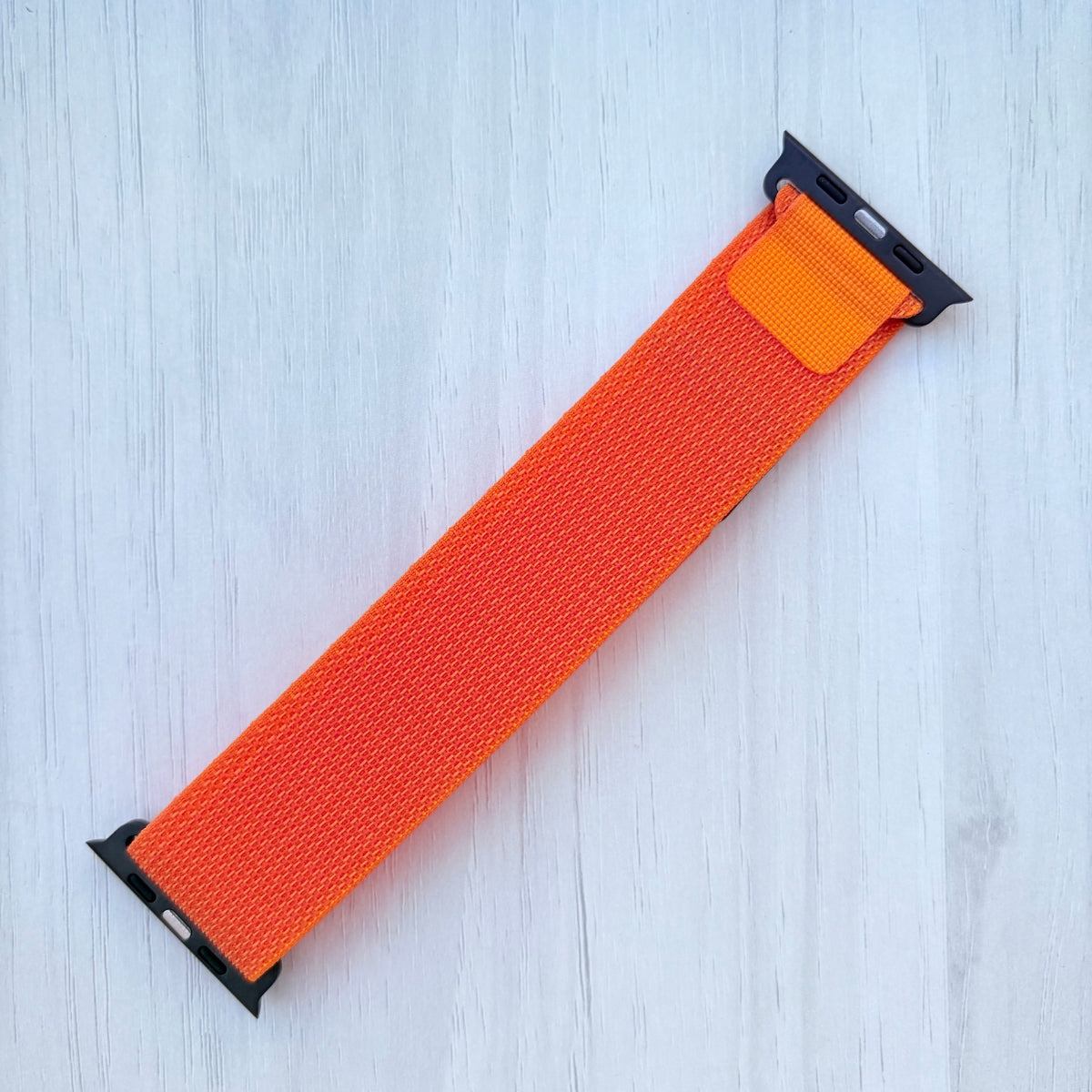 Orange Apple watch strap with black connectors on a white wooden background.