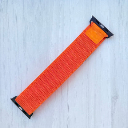 Orange Apple watch strap with black connectors on a white wooden background.