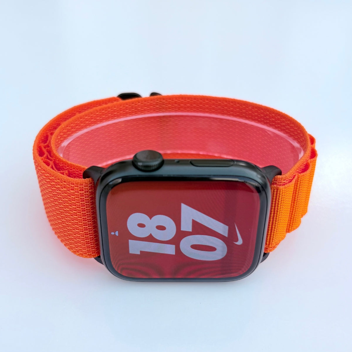 Face view Apple watch series 11 with Orange Alpine loop band with black connectors and buckle on a white background