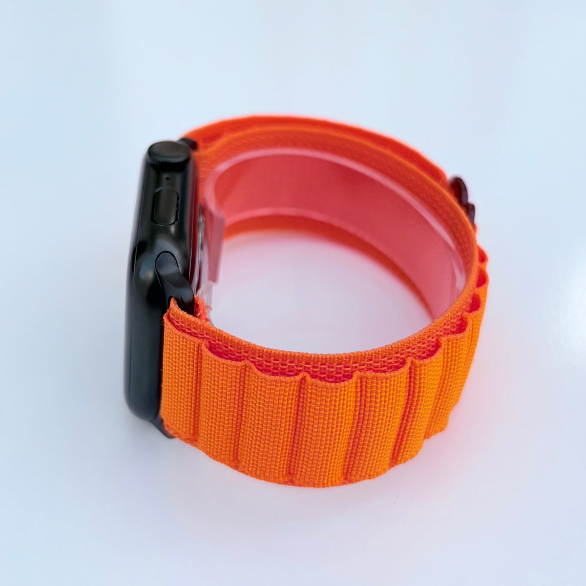 Side view Apple watch series 11 with Orange Alpine loop band with black connectors and buckle on a white background