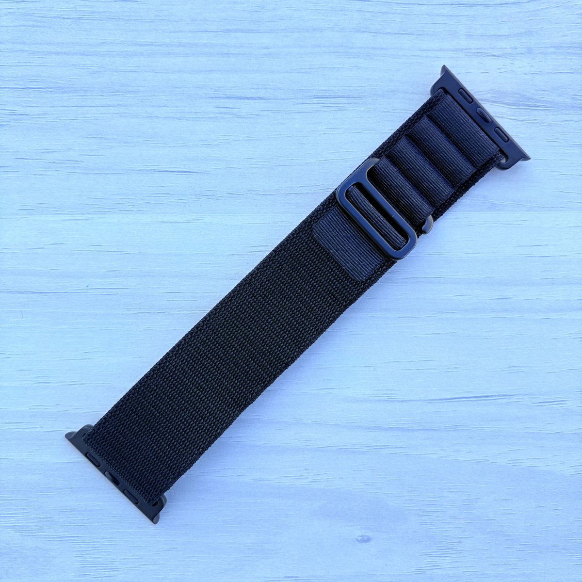 Black Alpine loop Band for apple watch with Black finish on a white wooden background front view