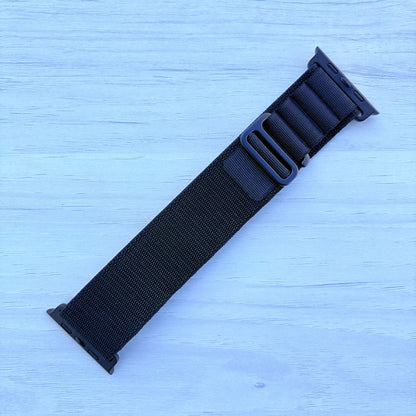 Black Alpine loop Band for apple watch with Black finish on a white wooden background front view