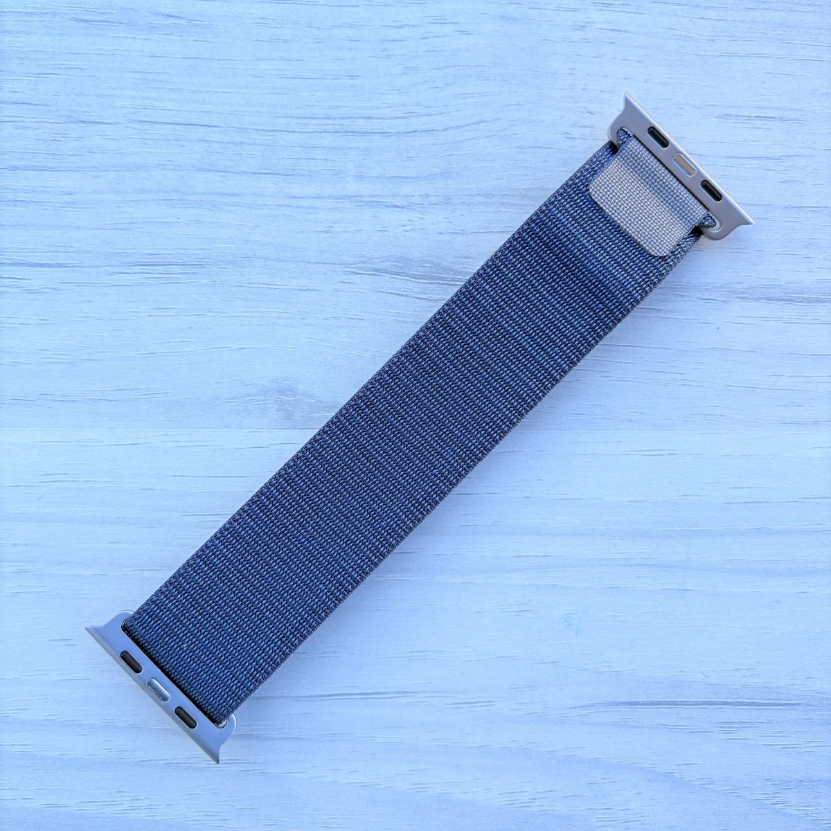 Blue Alpine Loop nylon band with titanium finish back view in a light white wooden background