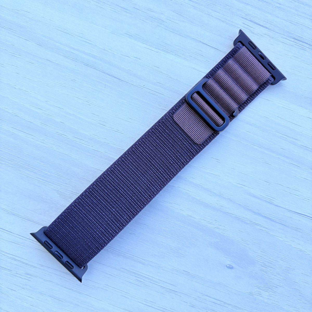 Indigo Alpine loop Band for apple watch with Black finish on a white wooden background front view