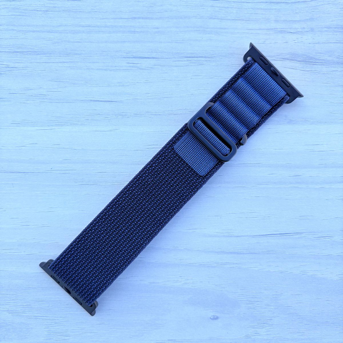 Navy blue Alpine loop Band for apple watch with Black finish on a white wooden background front view