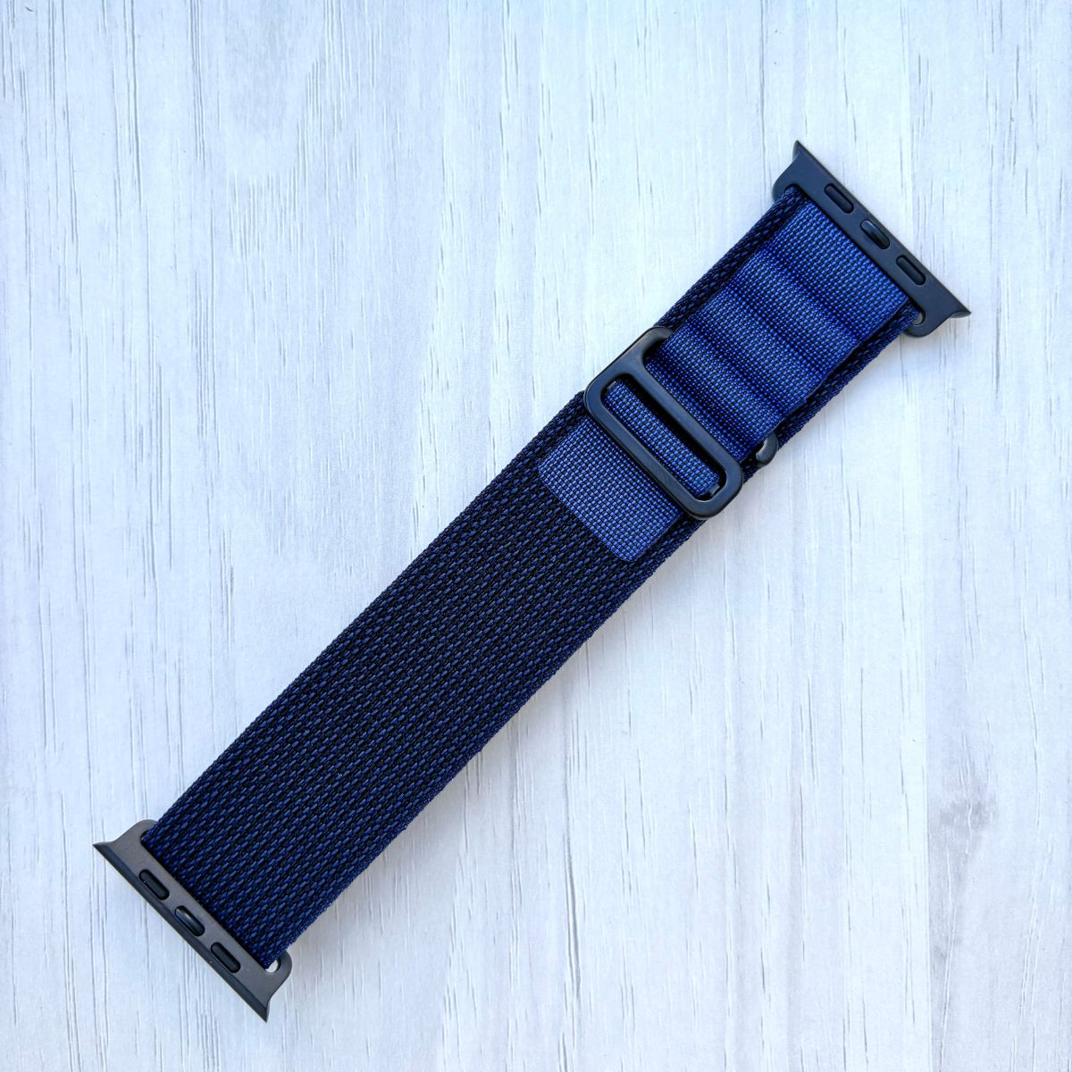 Navy Blue Apple watch strap with black hardware on a light wooden surface