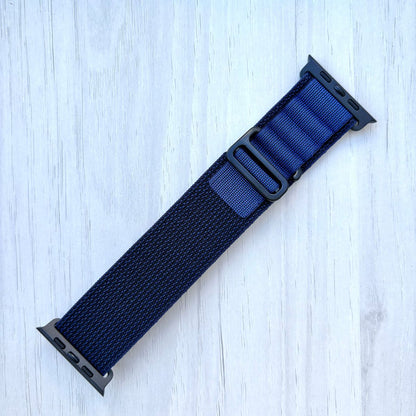 Navy Blue Apple watch strap with black hardware on a light wooden surface