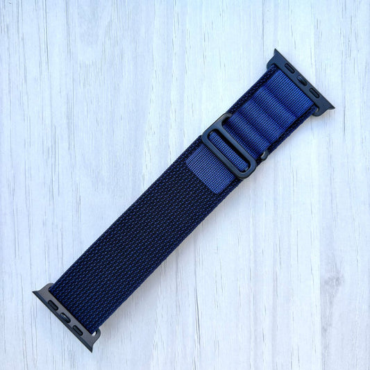 Navy Blue Apple watch strap with black hardware on a light wooden surface