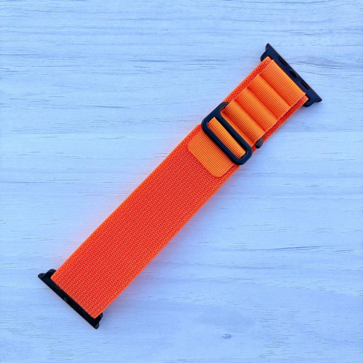 Orange Alpine loop Band for apple watch with Black finish on a white wooden background front view