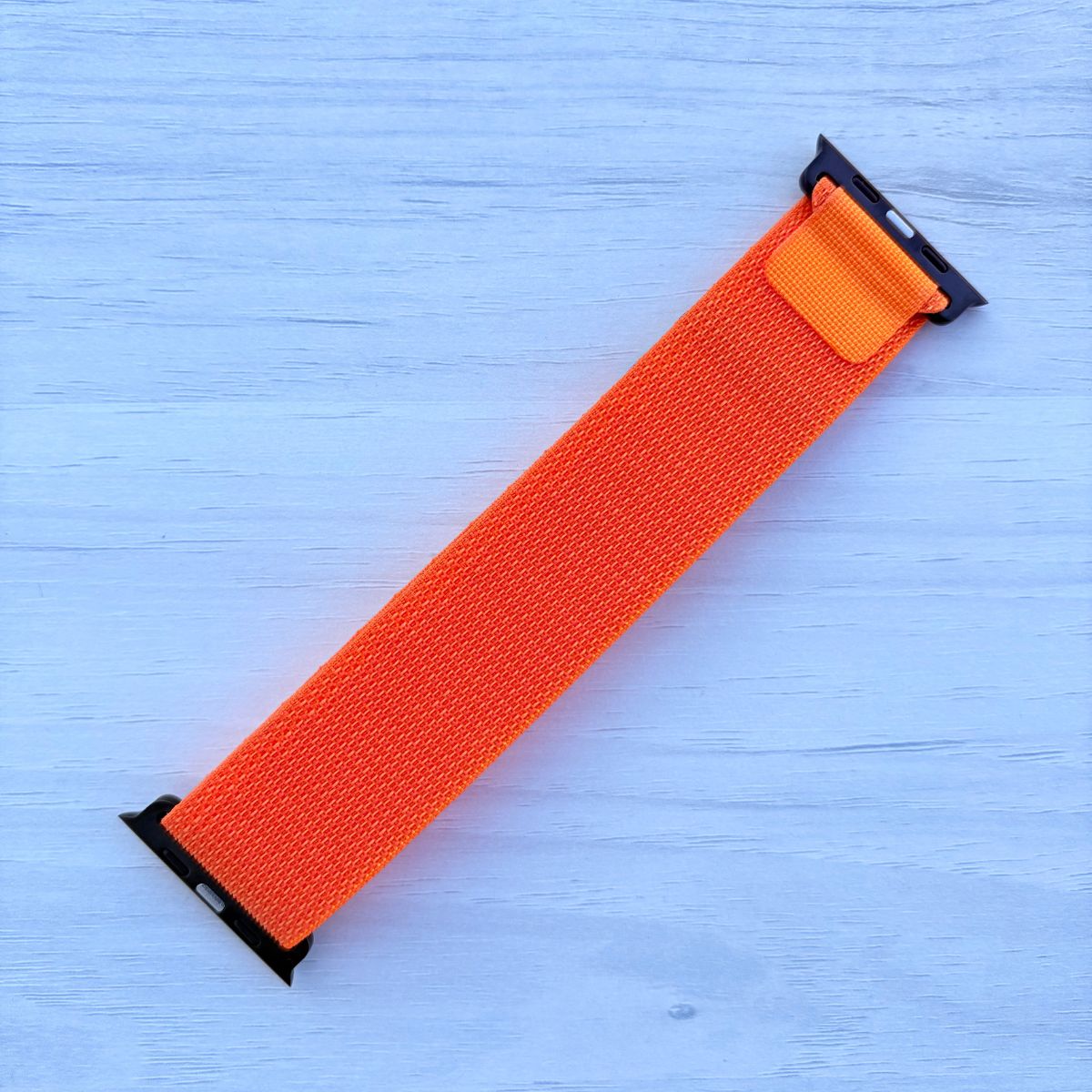 Orange Alpine loop Band for apple watch with Black finish on a white wooden background back view