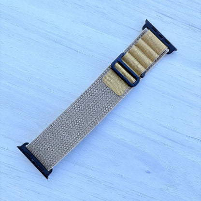 Tan Alpine loop Band for apple watch with Black finish on a white wooden background front view