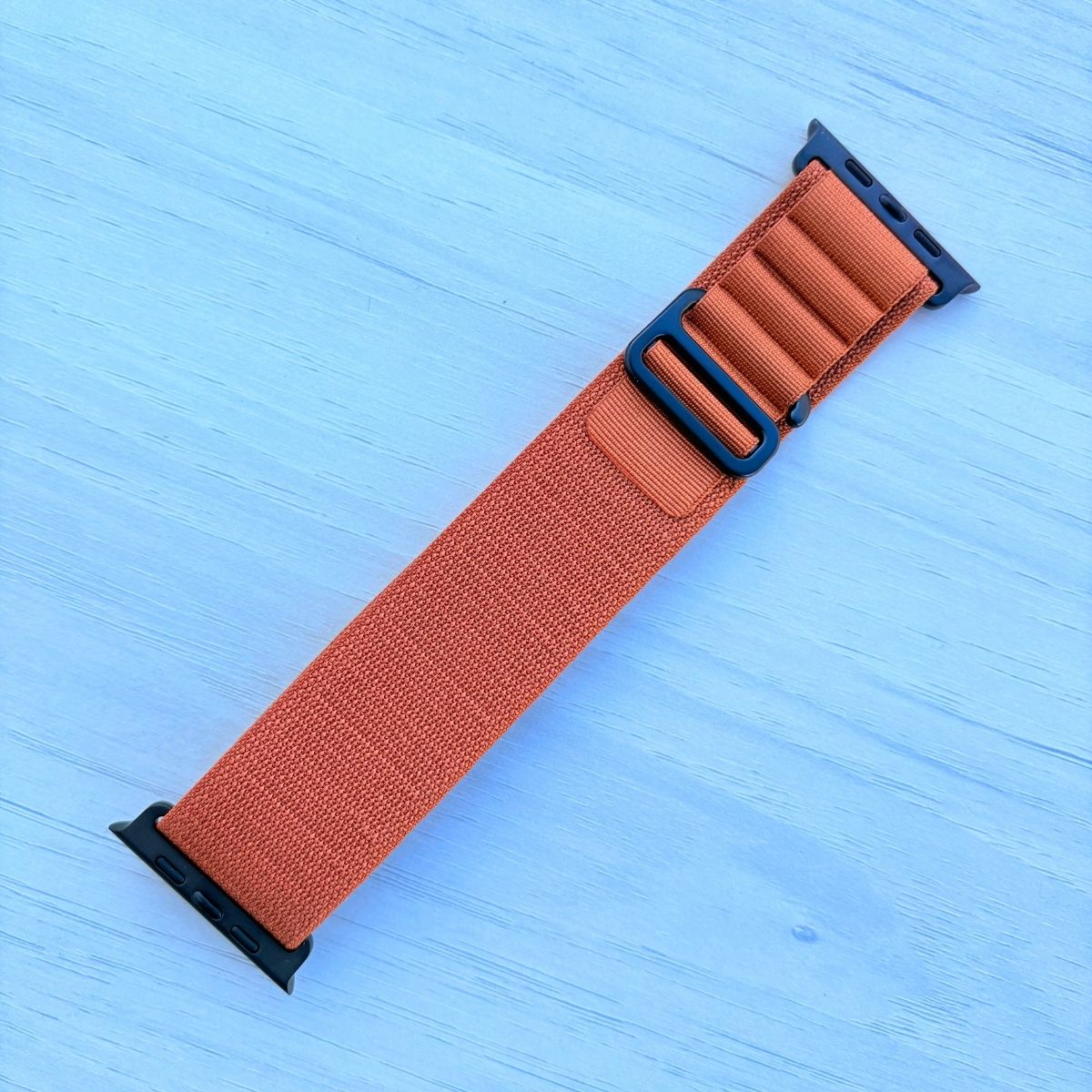 Terra Cotta Alpine loop Band for apple watch with Black finish on a white wooden background front view