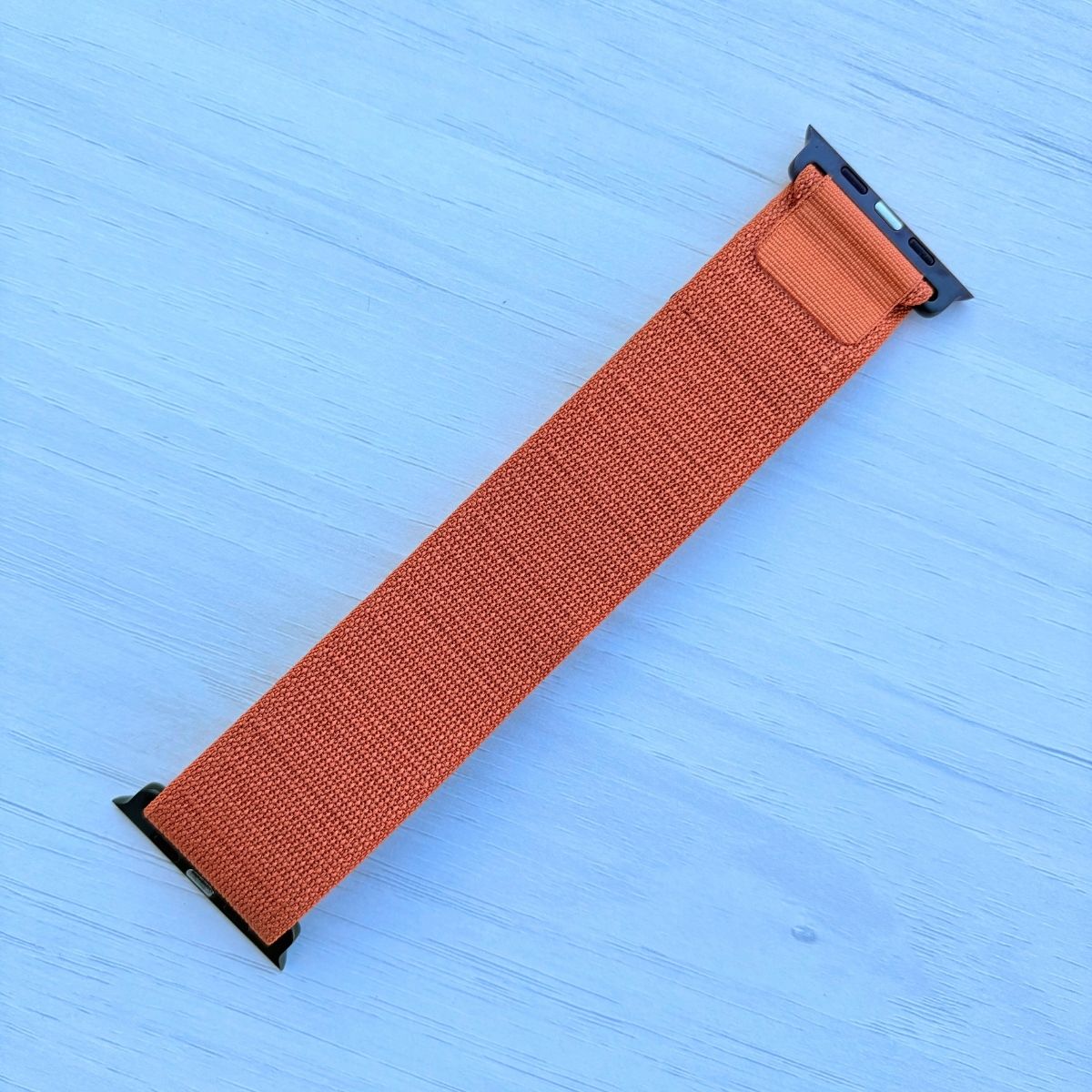 Terra Cotta Alpine loop Band for apple watch with Black finish on a white wooden background back view
