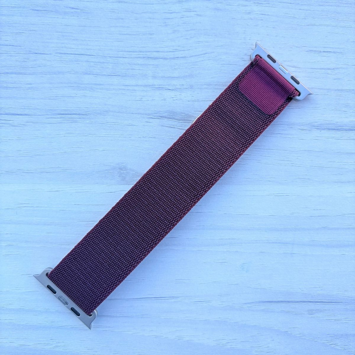Wine Red Alpine Loop band shown in a real back-side shot with a silver buckle, displayed on a light blue wooden surface
