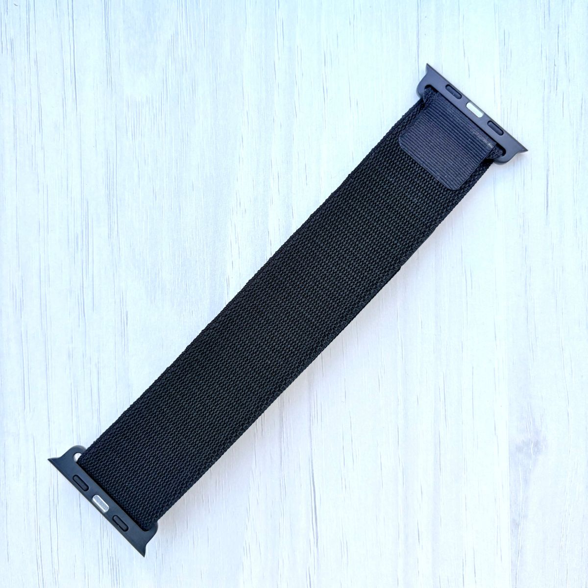 Black adjustable Alpine Loop Apple watch strap on a light blue wooden surface