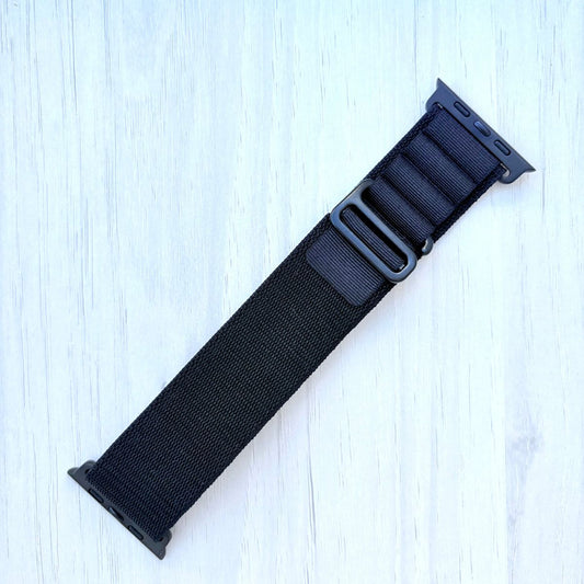 Black adjustable Alpine Loop Apple watch strap on a light blue wooden surface