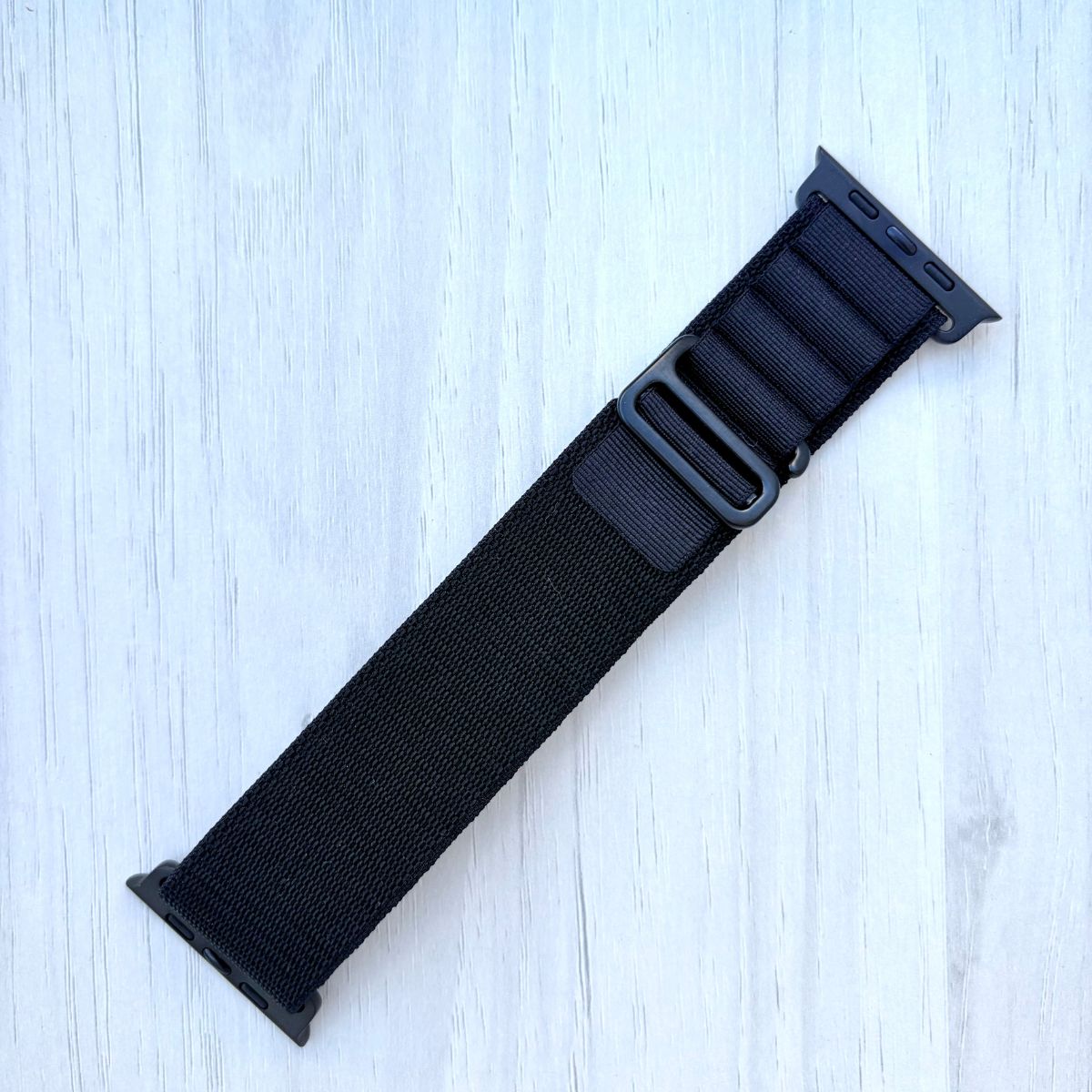 Black adjustable Alpine Loop Apple watch strap on a light blue wooden surface