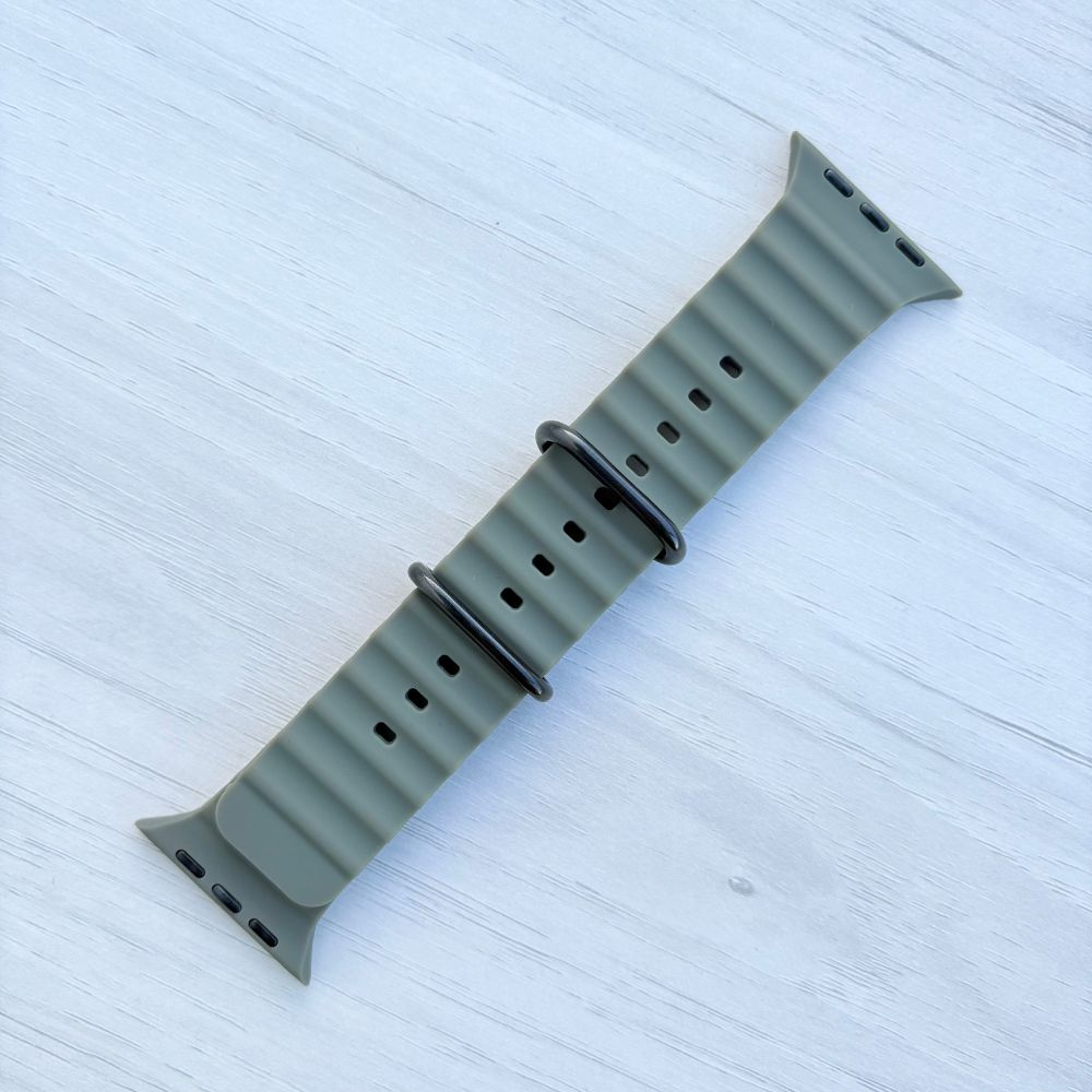Army green Ocean band Apple watch strap with black buckle on a light wooden surface