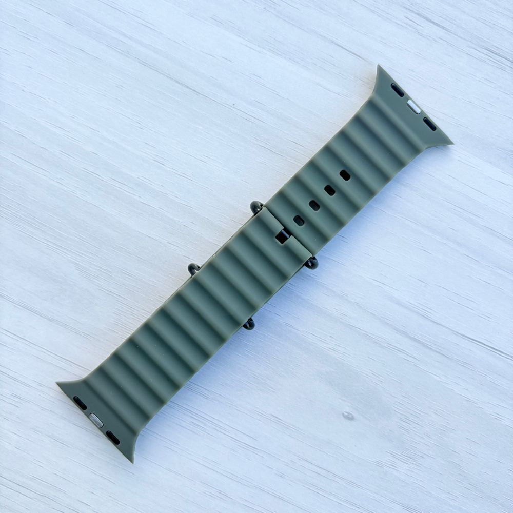 Army Green Ocean band Apple watch strap with black buckle back view on a light wooden surface
