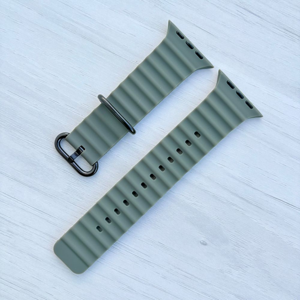 Green Ocean band Apple watch strap with black buckle on a light wooden surface