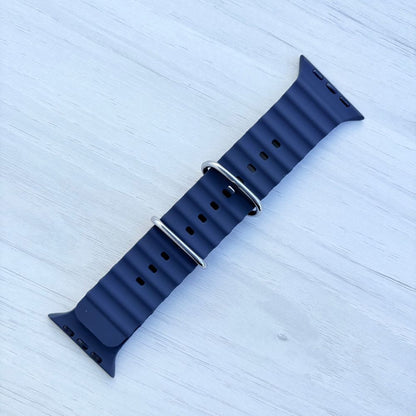 Black Ocean band Apple watch strap with silver buckle front view on a light wooden surface