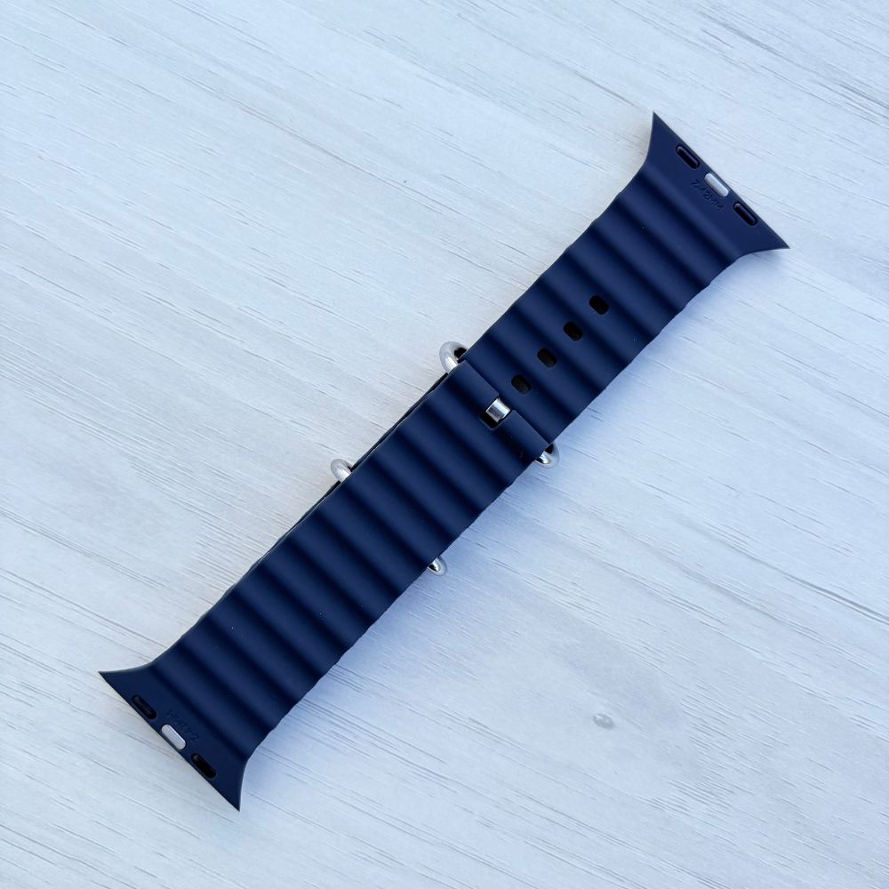 Black Ocean band Apple watch strap with silver buckle Back view on a light wooden surface