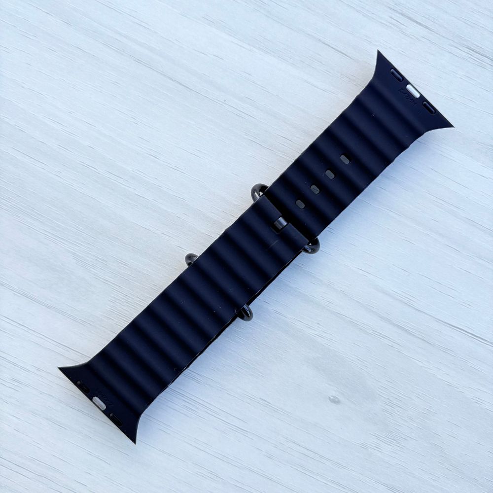 Black Ocean band Apple watch strap with black buckle back view on a light wooden surface
