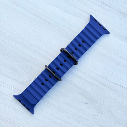 Ocean band for Apple watch in midnight blue with Black buckle on a light wooden surface front view.