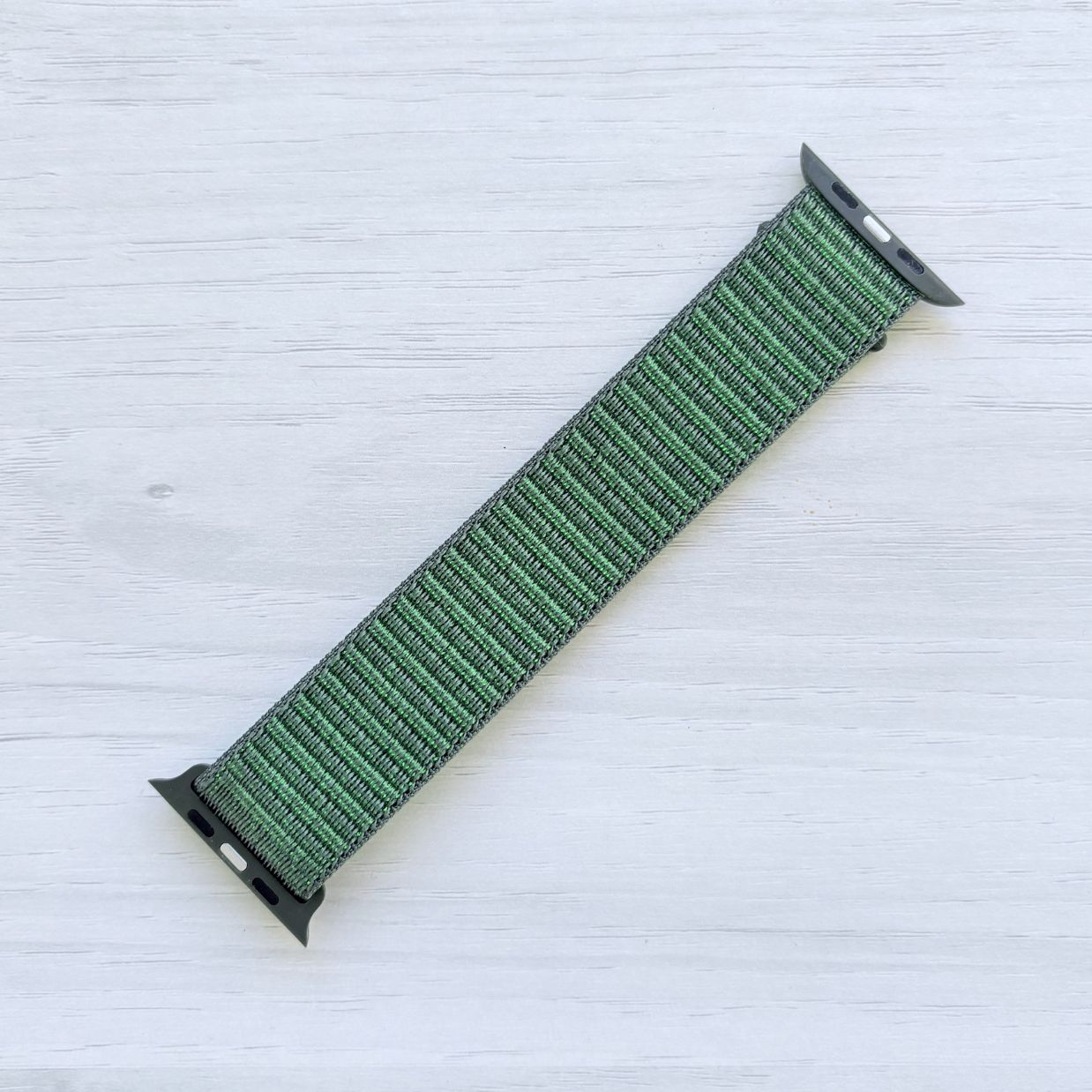 Agate Green Sport Loop Apple Watch Band with woven nylon design displayed on a light wooden surface, back view.