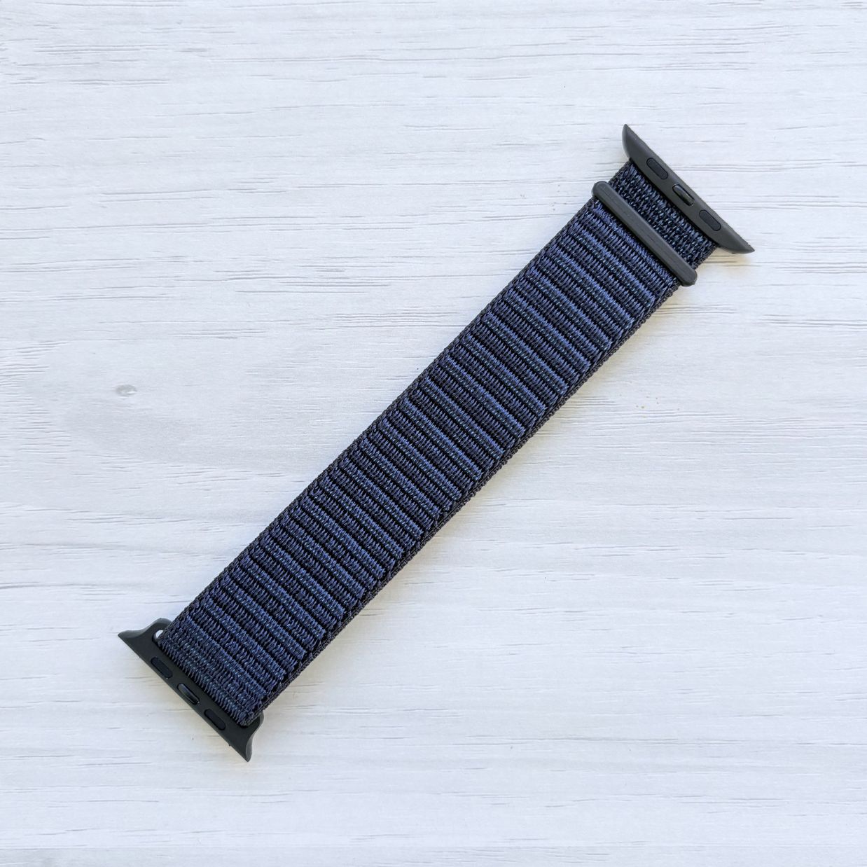 Ink Sport Loop Apple Watch Band with woven nylon design displayed on a light wooden surface, front view.