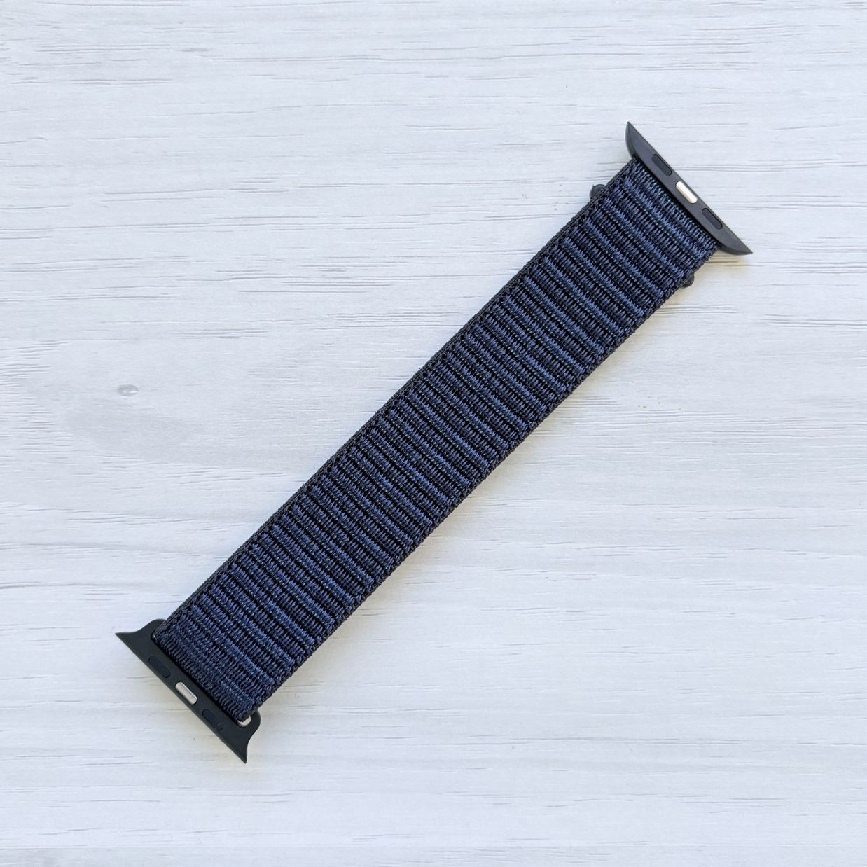 Ink Sport Loop Apple Watch Band with woven nylon design displayed on a light wooden surface, back view.