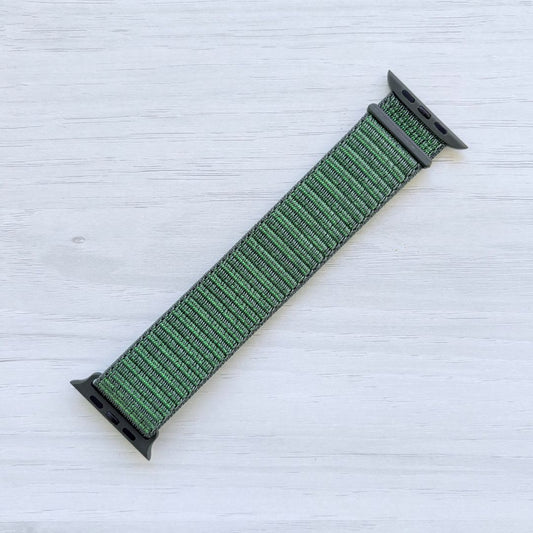 Sage nylon sport loop Apple watch strap with green hardware on a light wooden surface